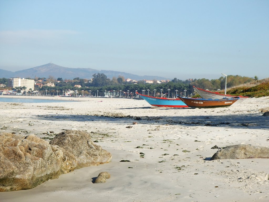 Playa de Samil con barcas de madera varadas en la arena y el paseo al fondo