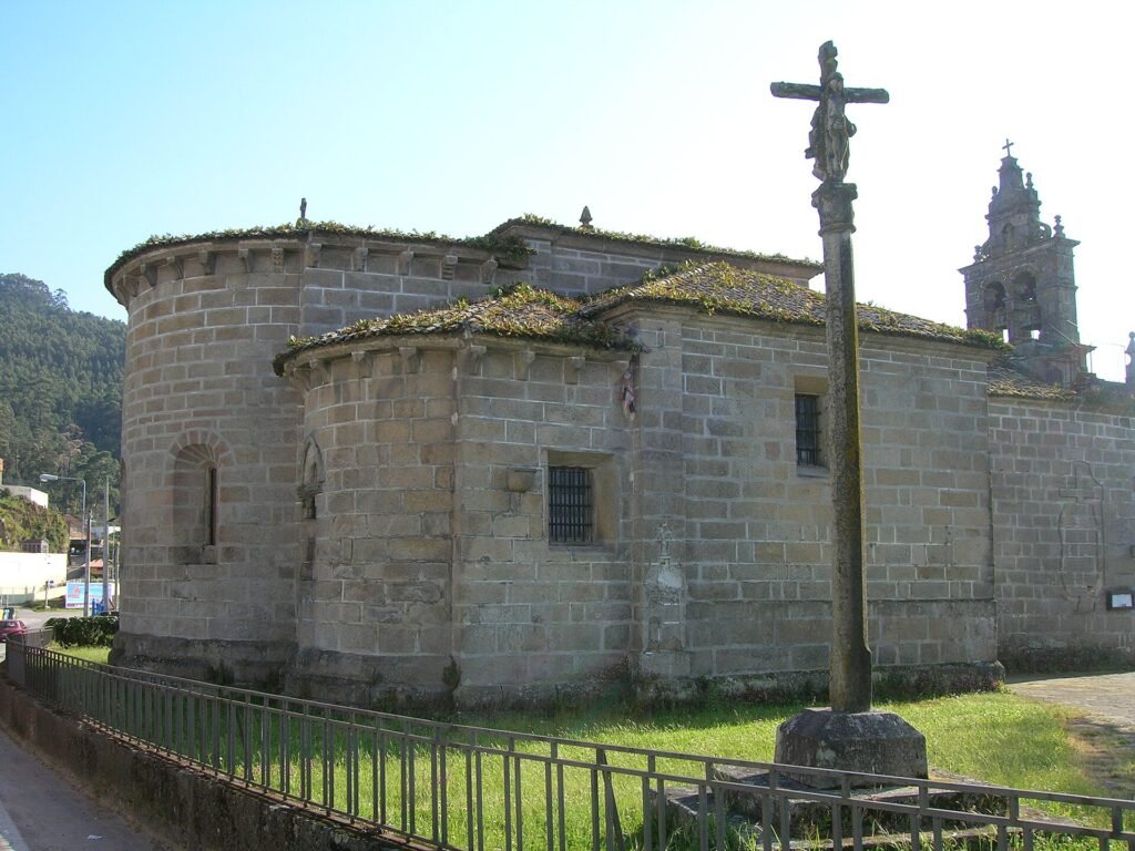 Ábsides románicos de la iglesia de San Salvador de Coruxo con un cruceiro en primer plano