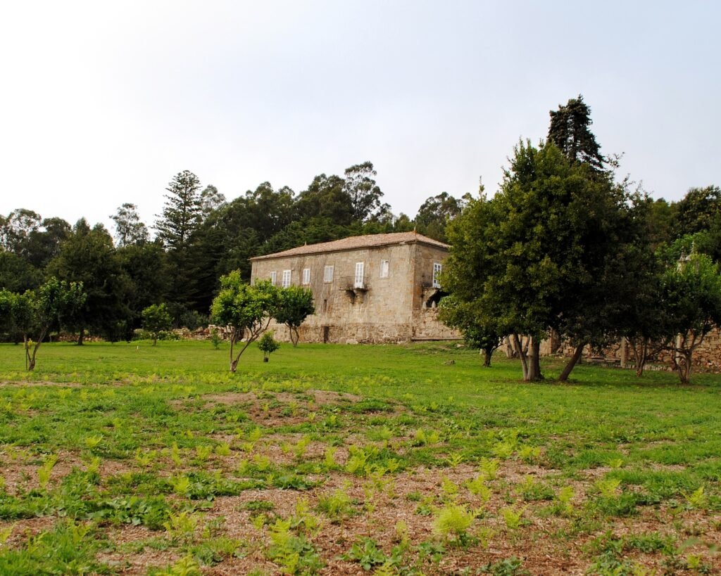 Pazo de Cea entre naranjos y prado, con el monte al fondo